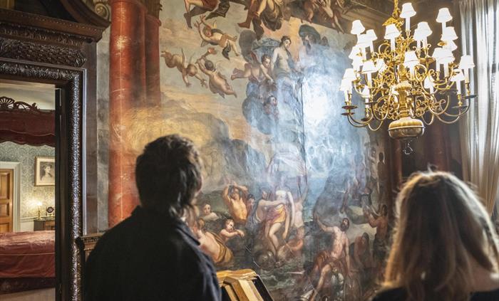 Visitors looking at the walls of the grand staircase which is covered in intricate paintings